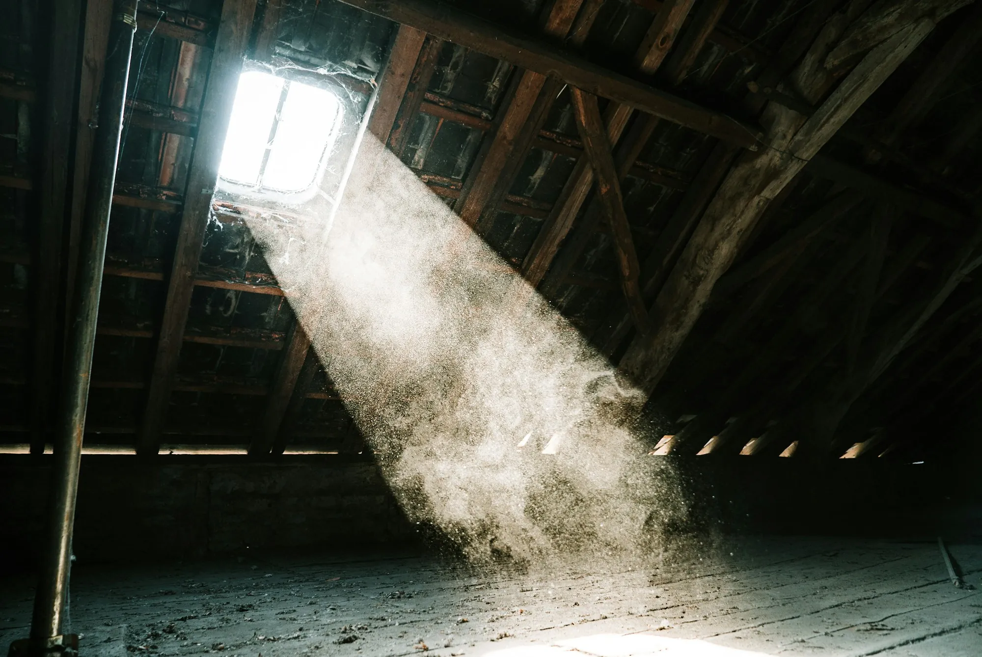 Beam of sunlight shining through a roof opening into a dusty attic